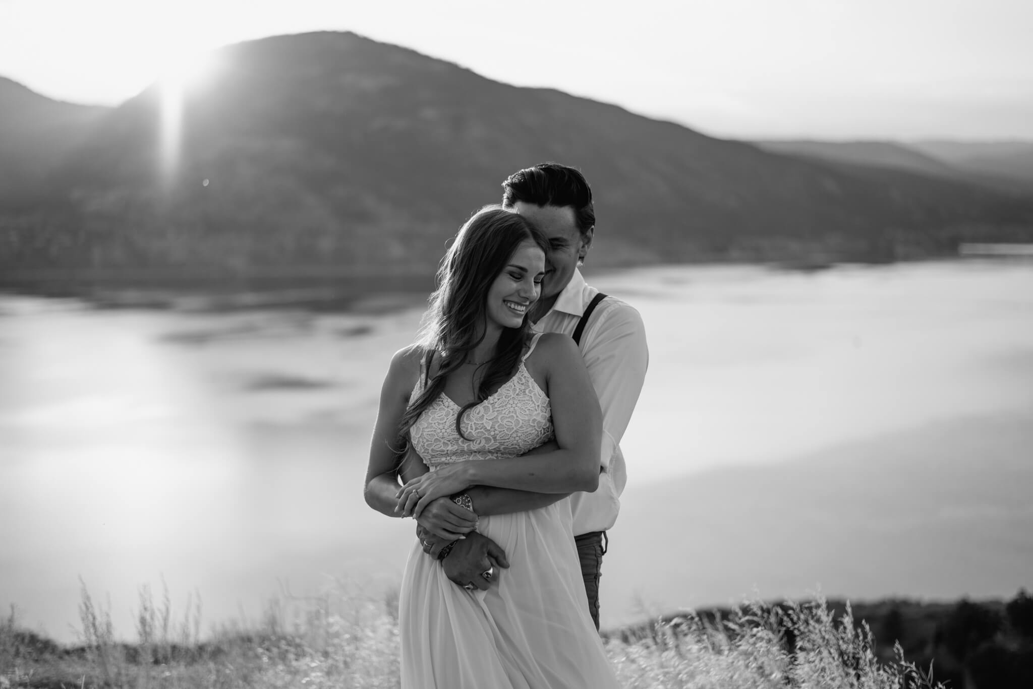 husband hugs wife from behind in b&w photo